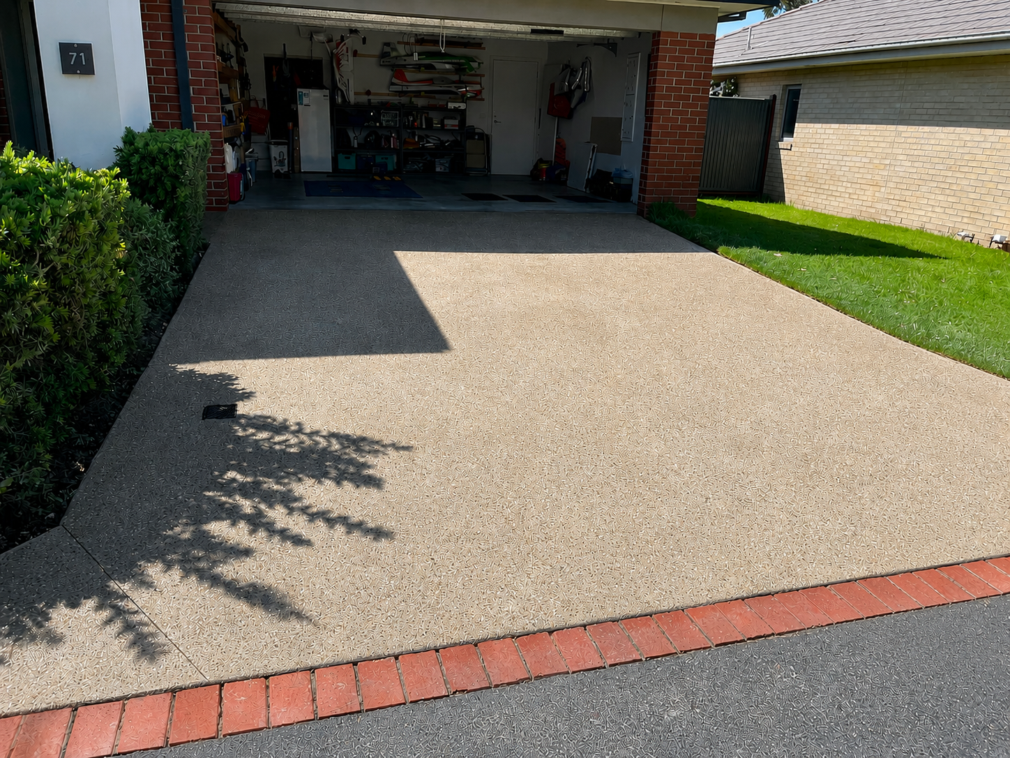 Exposed aggregate concrete driveway with red brick edging leading to a residential garage.