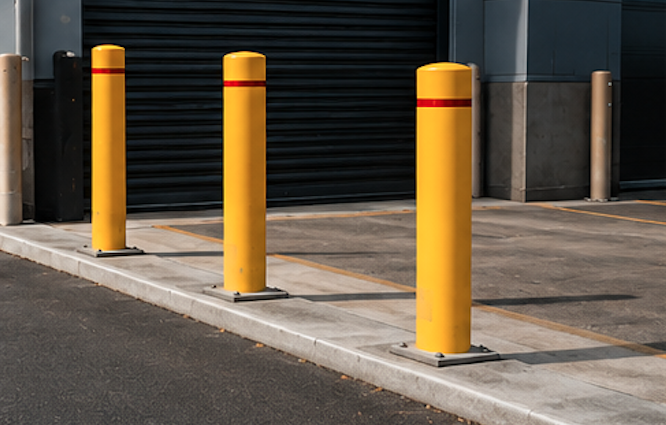 Three yellow safety bollards with red reflective bands installed in front of a roller door at a warehouse loading area.