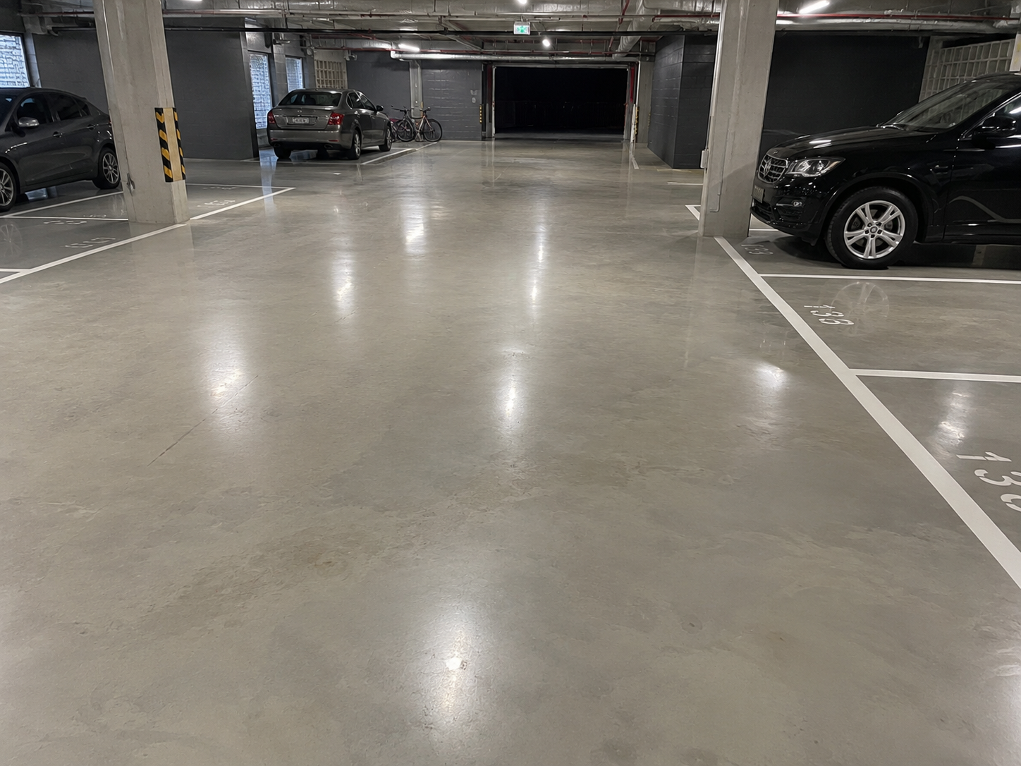 Epoxy-sealed grey carpark floor with crisp white line marking, bay numbers and directional arrow.