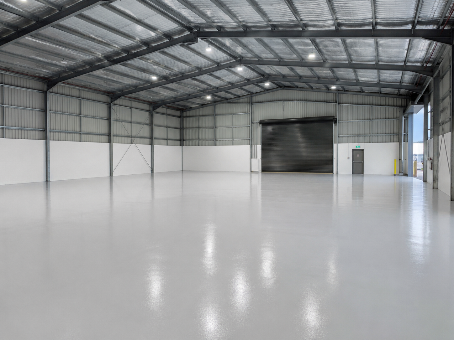 Large industrial warehouse interior with a fresh light-grey epoxy floor coating reflecting overhead lighting.